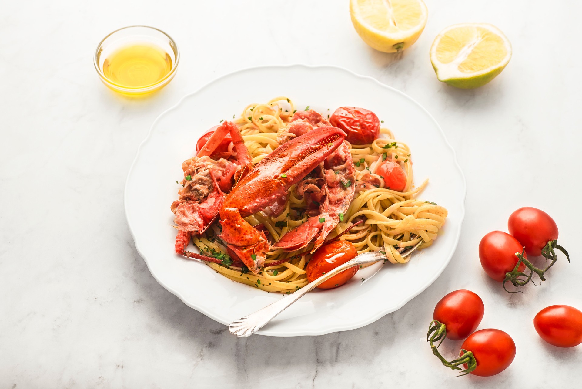 Lobster linguine  pasta   with ingredients for cooking. Lemon, tomatoes, olive oil, parsley on the white marble  table. Delicatessen, rare seafood pasta recipe. Sardinia, Sicilian, Neapolitan cuisine. Italian and French food. Front view